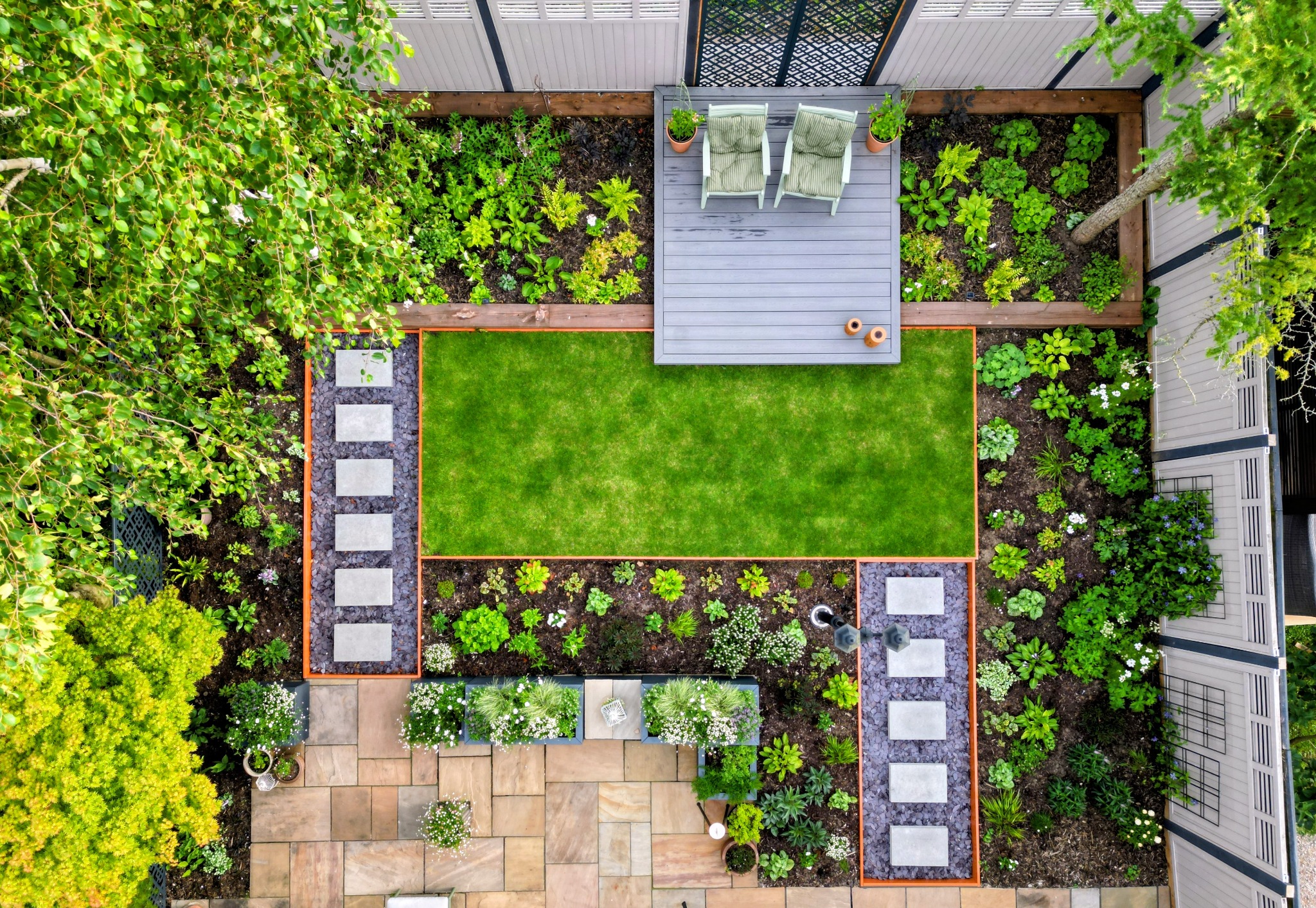 Overhead view of a garden with lawn, planted borders, concrete stepping stones and a raised seating deck